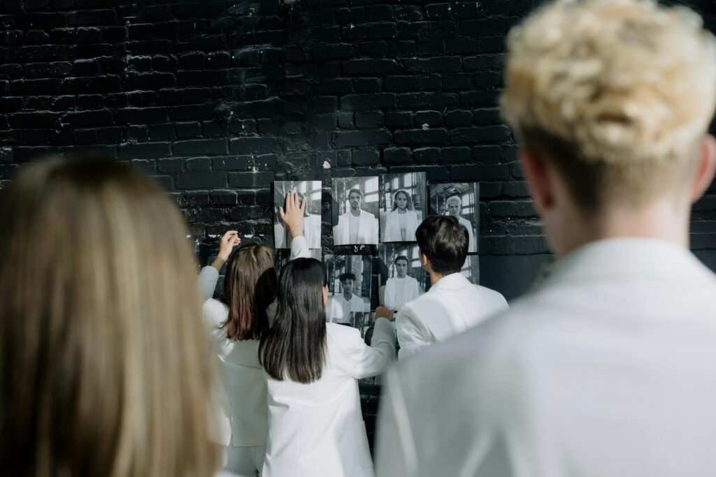 People in white clothing analyzing black and white photos on a brick wall.