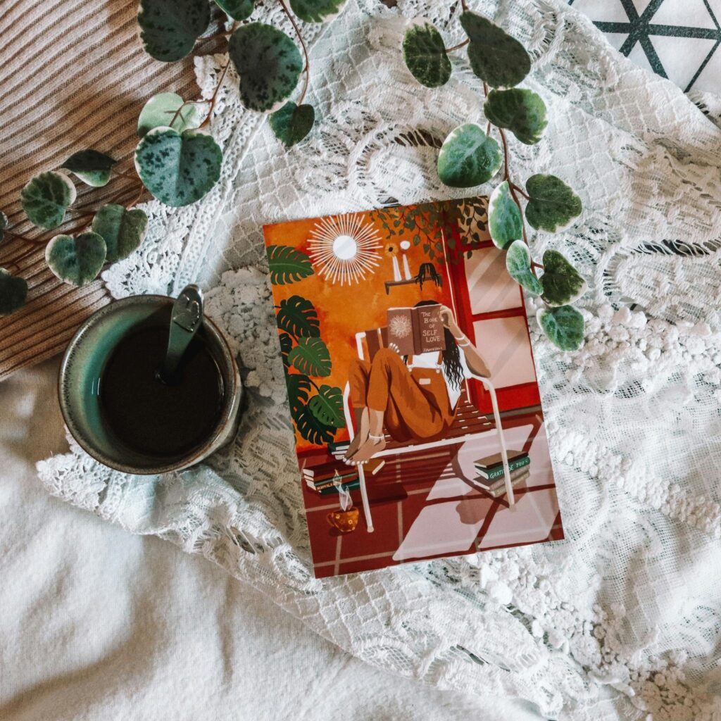 A cozy overhead view of chamomile tea, green leaves, and artistic poster on white fabric.