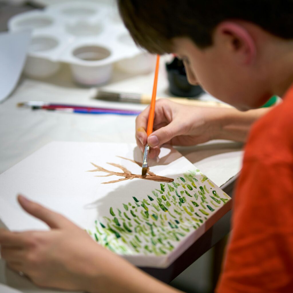 A young boy paints a tree on canvas, showcasing creativity and focus indoors.