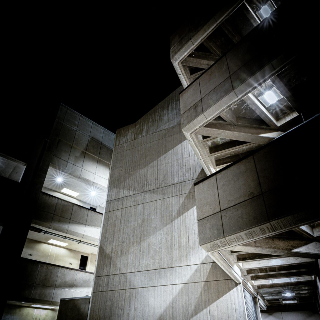A striking low angle view of modern concrete buildings against the night sky, showcasing unique geometric designs and lighting.