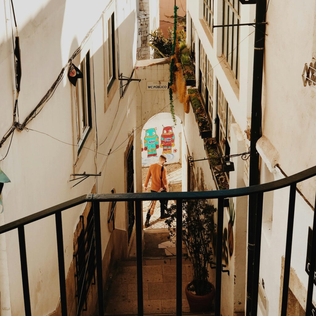 A picturesque view of a Lisbon alleyway with street art and warm sunlight casting shadows.