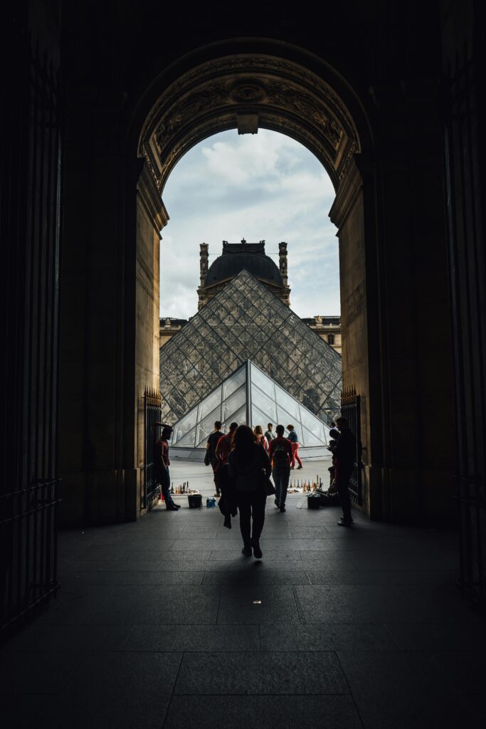 Visitors silhouette at the Louvre Pyramid entrance in Paris on a sunny day.