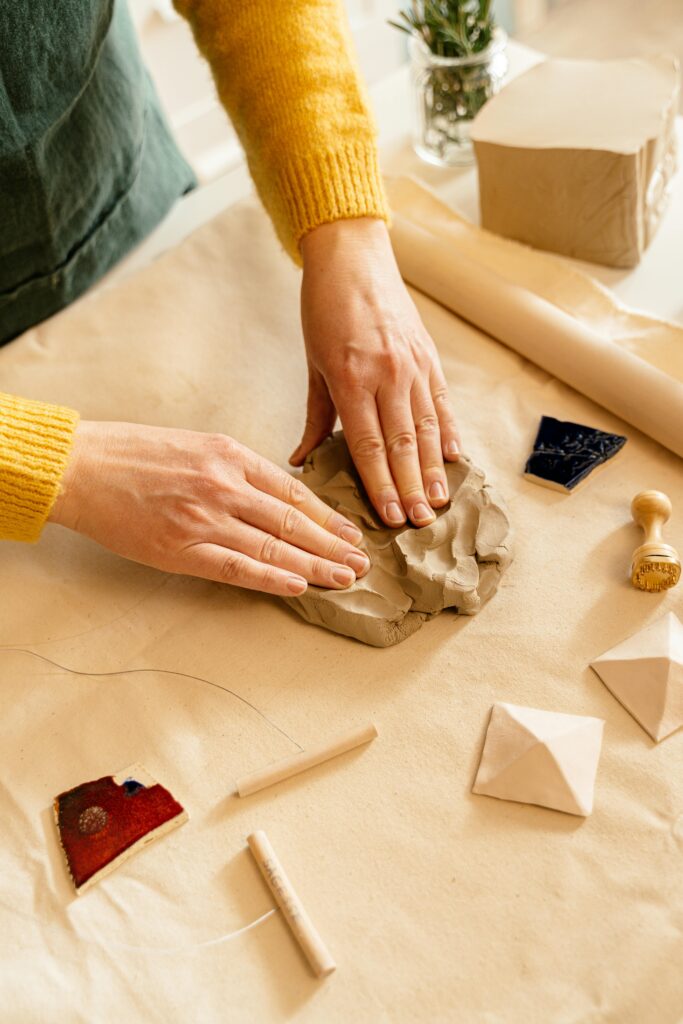Close-up of hands molding clay on a work table with tools, showcasing artisan craftsmanship.